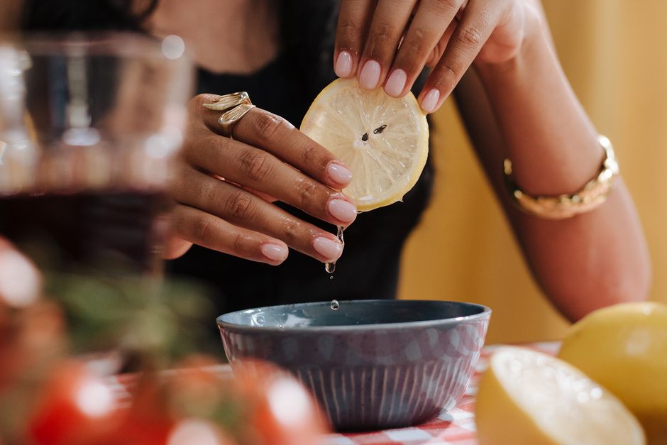 Femme pressant un citron au-dessus d'un bol, avec des bagues aux doigts, sur une table à carreaux.