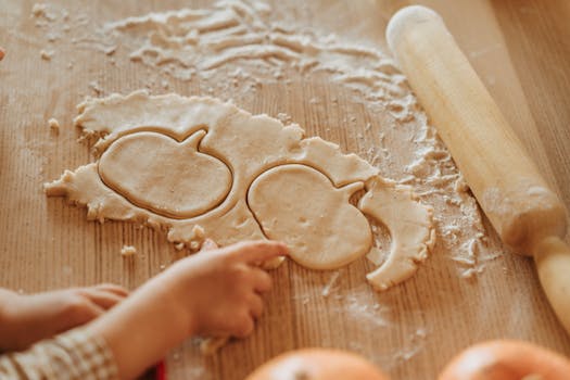 Enfant découpant des formes de pâte à biscuits sur une table en bois avec un rouleau à pâtisserie.