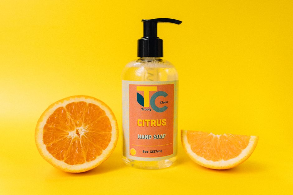 Flacon de savon liquide aux agrumes avec des oranges coupées sur fond jaune, idéal pour éliminer les odeurs en cuisine.