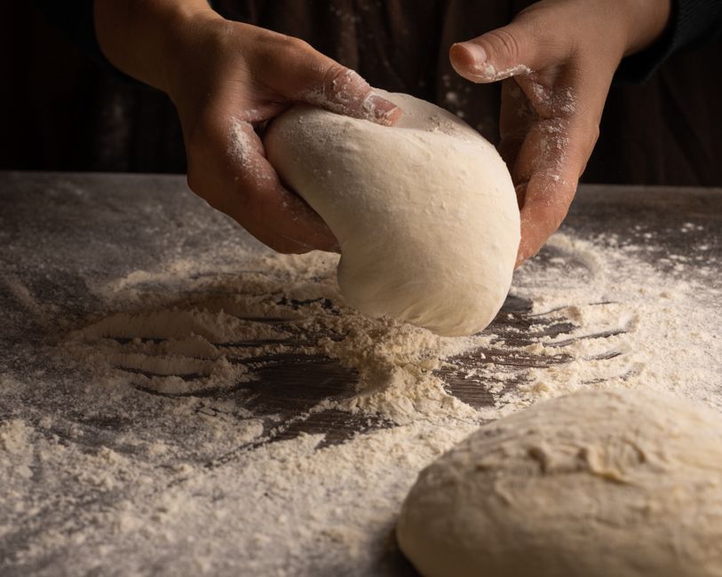 Mains pétrissant une pâte à pain sur un plan de travail fariné, sans résidu sur les doigts.