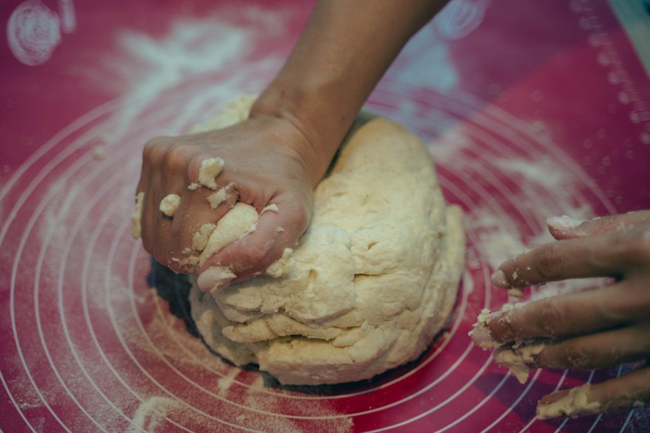 Main pétrissant une pâte sur un plan de travail, sans résidu de pâte sur les doigts, avec de la farine autour.