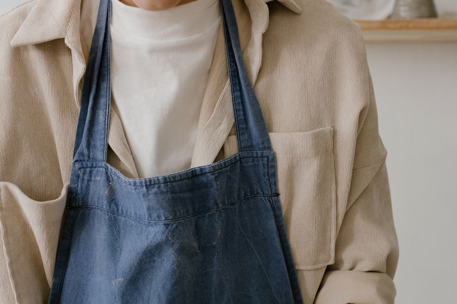 Personne portant un tablier en denim, avec un haut clair, dans un espace de travail minimaliste.