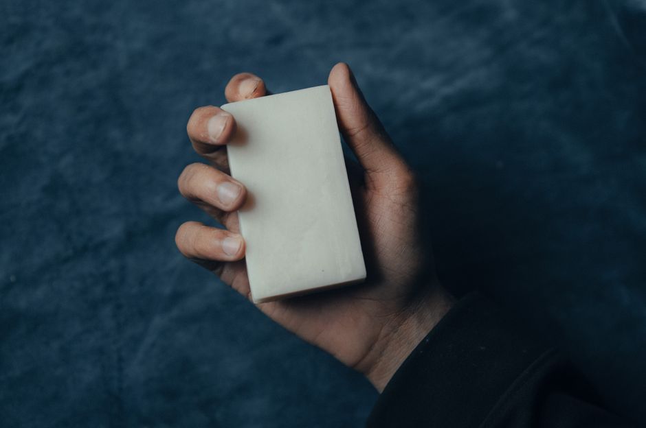 Main tenant un morceau de savon blanc sur un fond sombre, illustrant des astuces pour enlever les odeurs tenaces.