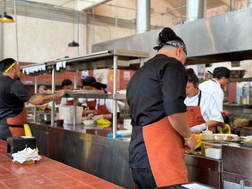 Cuisiniers en action dans une cuisine ouverte, préparant des plats avec des tabliers et des ustensiles.